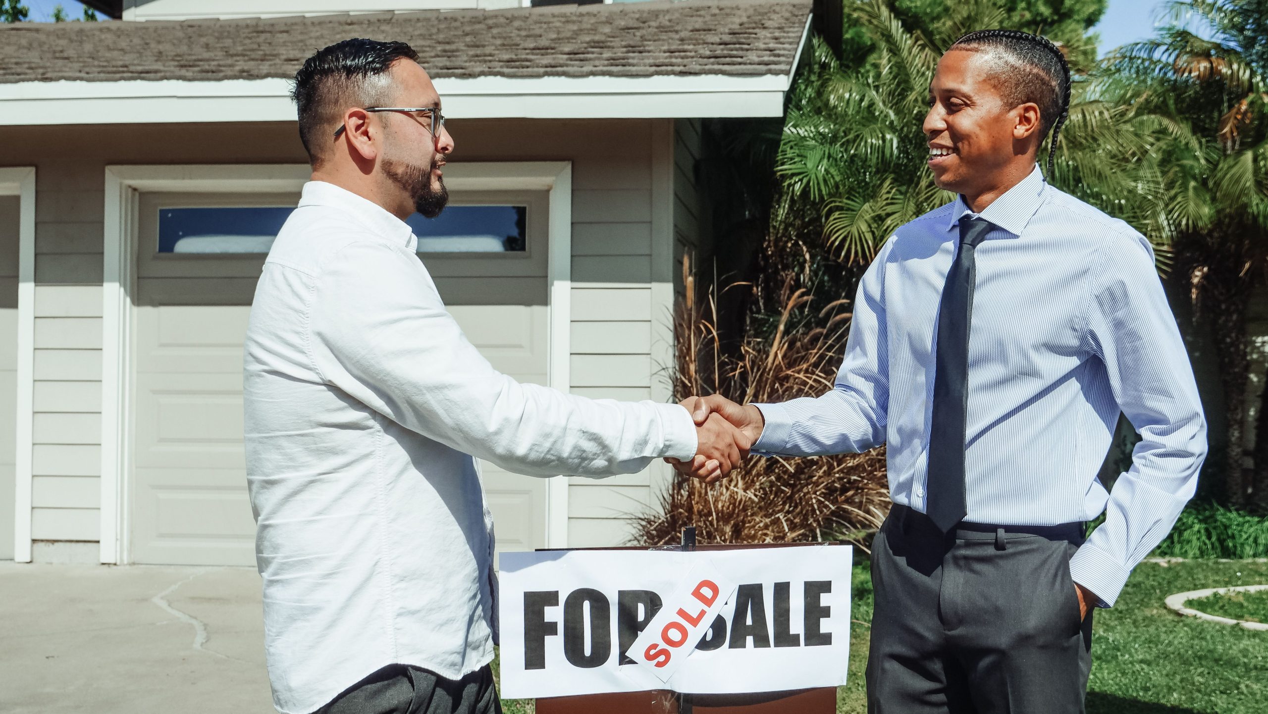 realtor and homebuyer shaking hands, with 'sold' signage between them